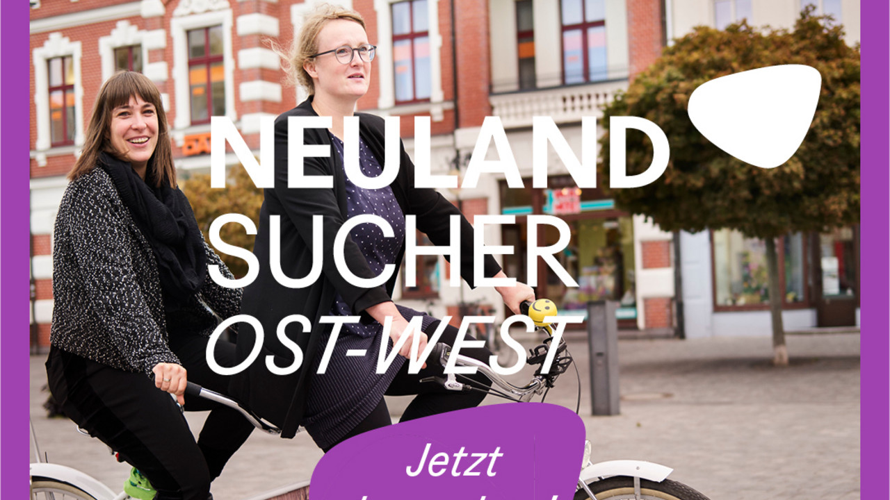 Keyvisual Neulandsucher: zwei Frauen, auf einem Tandem fahrend, lächeln in die Kamera